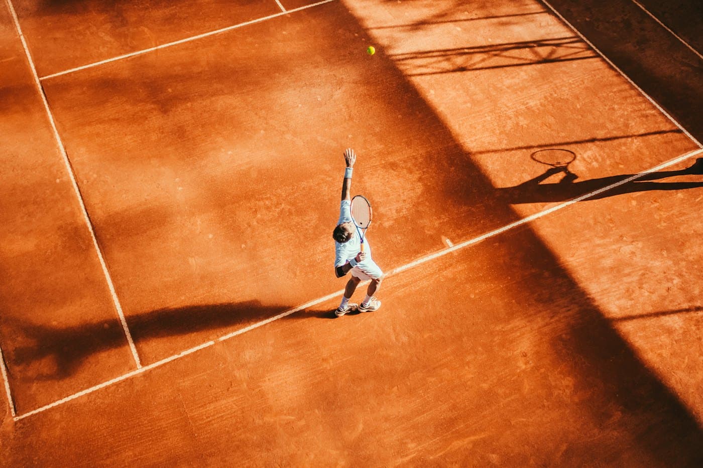 A tennis player serving on a clay court, seen from above